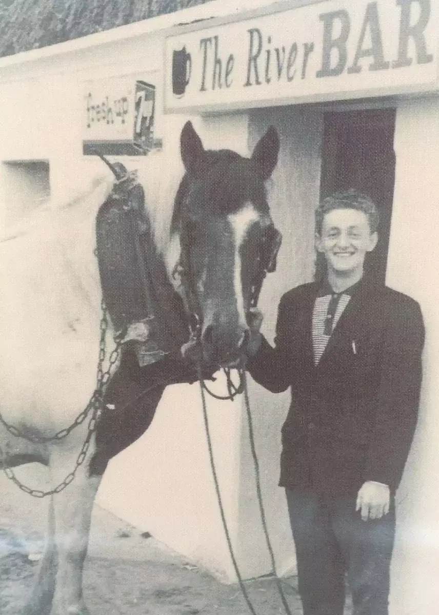 A young man standing with a horse outside of a bar.