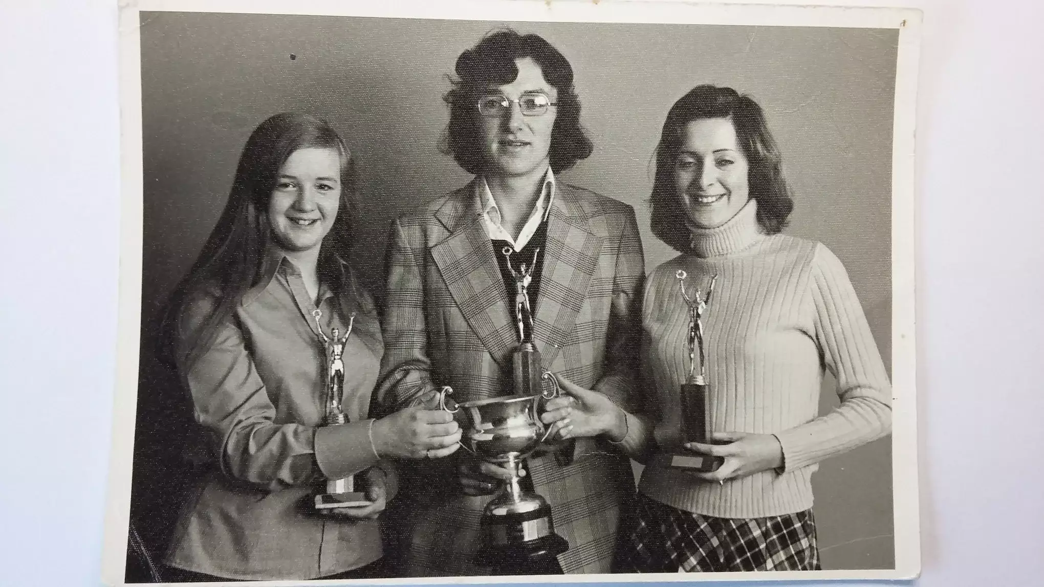 A man standing between two women holding trophies.